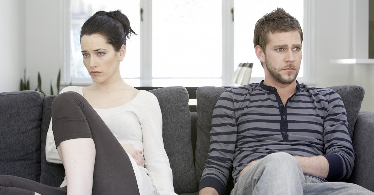 Couple sitting on sofa looking angry, touching hands